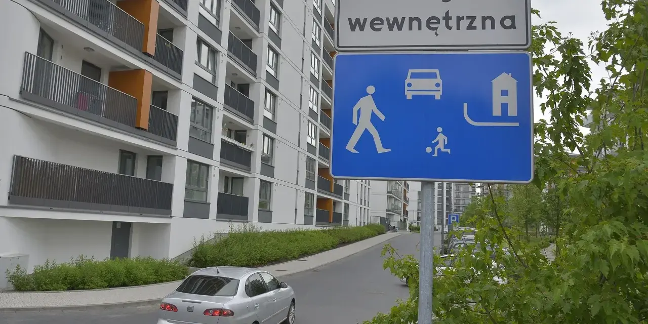 Droga wewnętrzna w terenie zabudowanym. Znak informuje o ruchu pieszych, samochodów i domów.