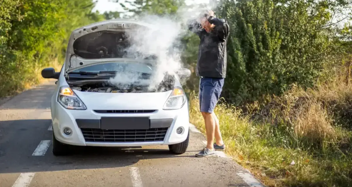 Rozbiegany diesel dymi spod maski. Mężczyzna w rozpaczy łapie się za głowę, stojąc przy białym samochodzie na poboczu drogi.