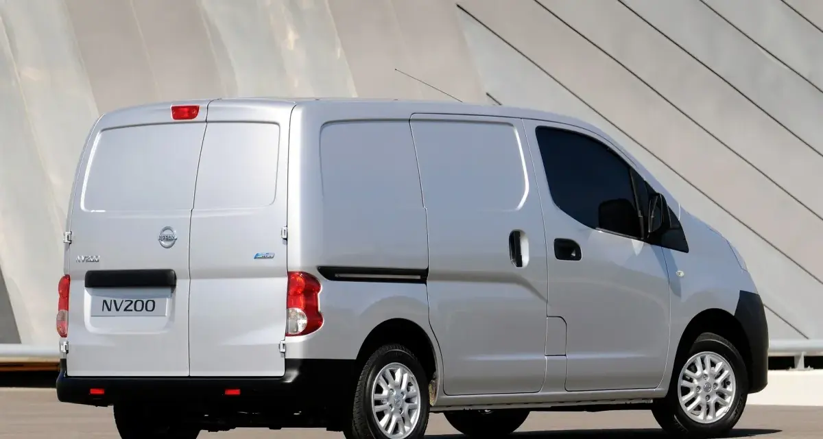 Srebrny Nissan NV200, wszechstronny van, zaparkowany przed nowoczesnym budynkiem.
