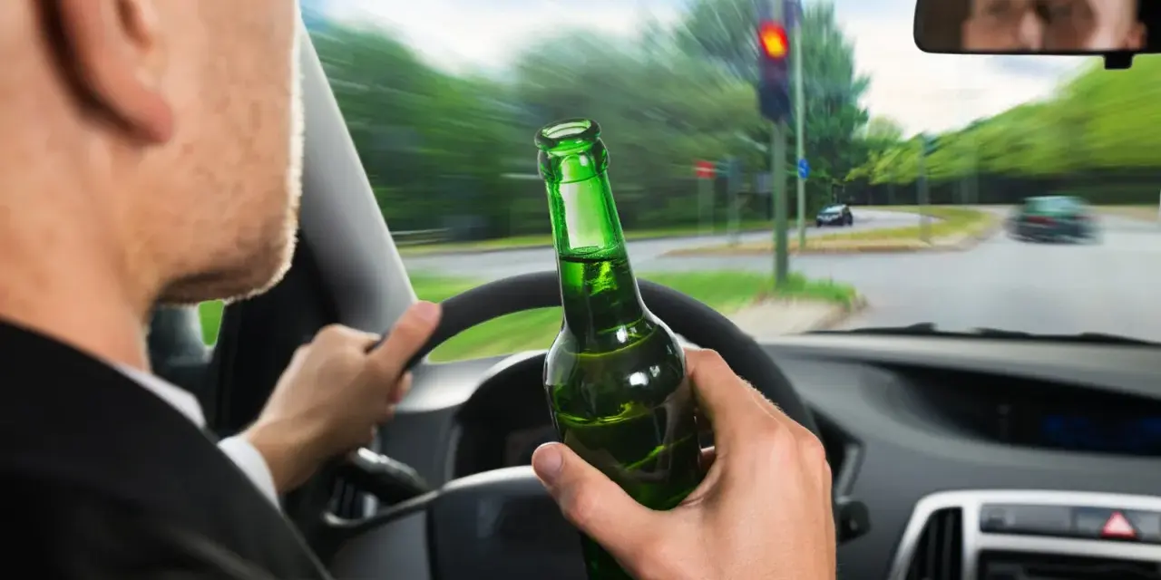 Kierowca z butelką piwa w ręku, jadący na czerwonym świetle. Grozi mu konfiskata samochodu.