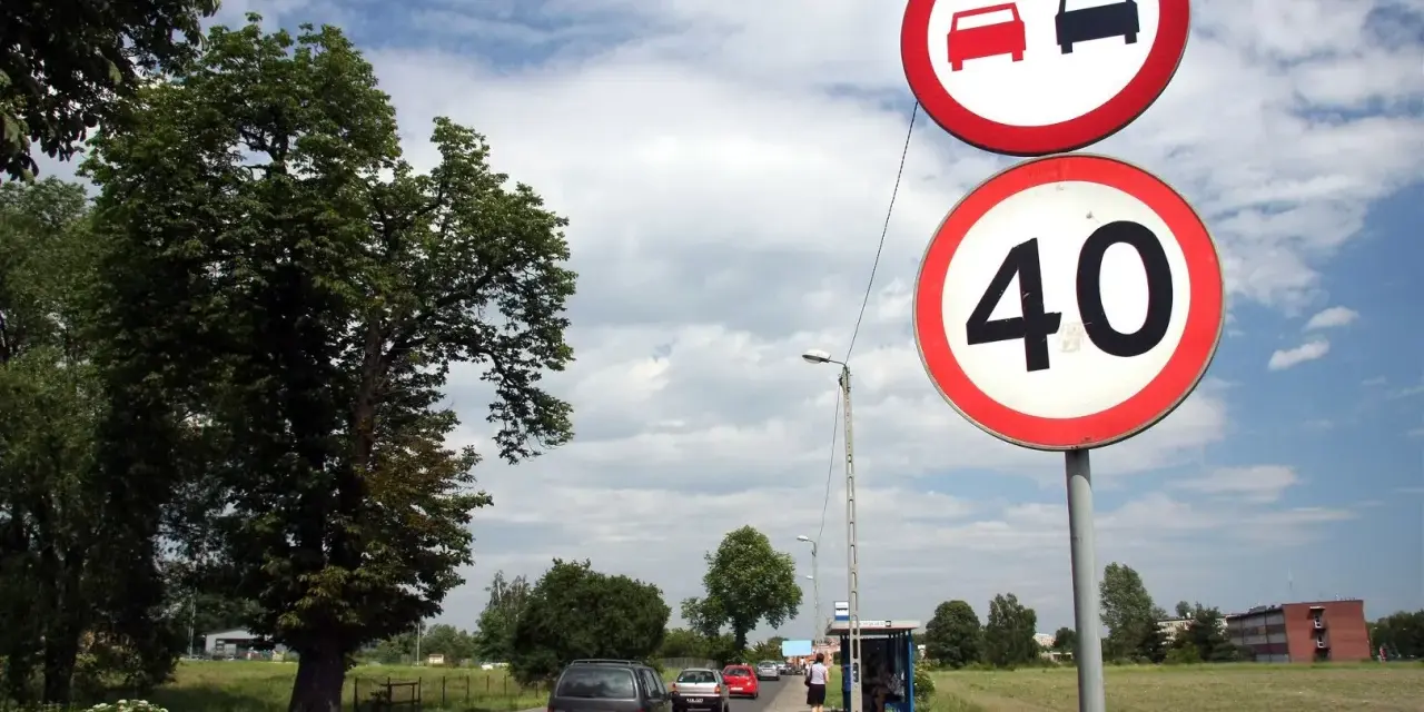 Znaki drogowe: zakaz wyprzedzania i ograniczenie prędkości do 40 km/h. Droga z samochodami i drzewami.