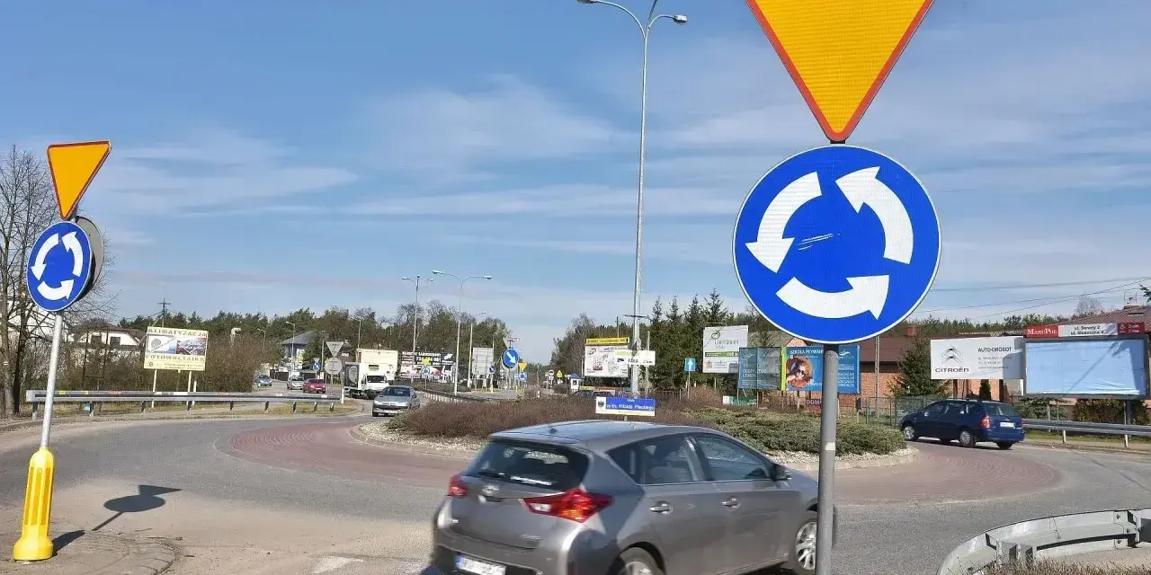 Rondo z tablicami "ustąp pierwszeństwa" i "ruch okrężny". Kierowca w szarym samochodzie może dostać mandat za wymuszenie pierwszeństwa.