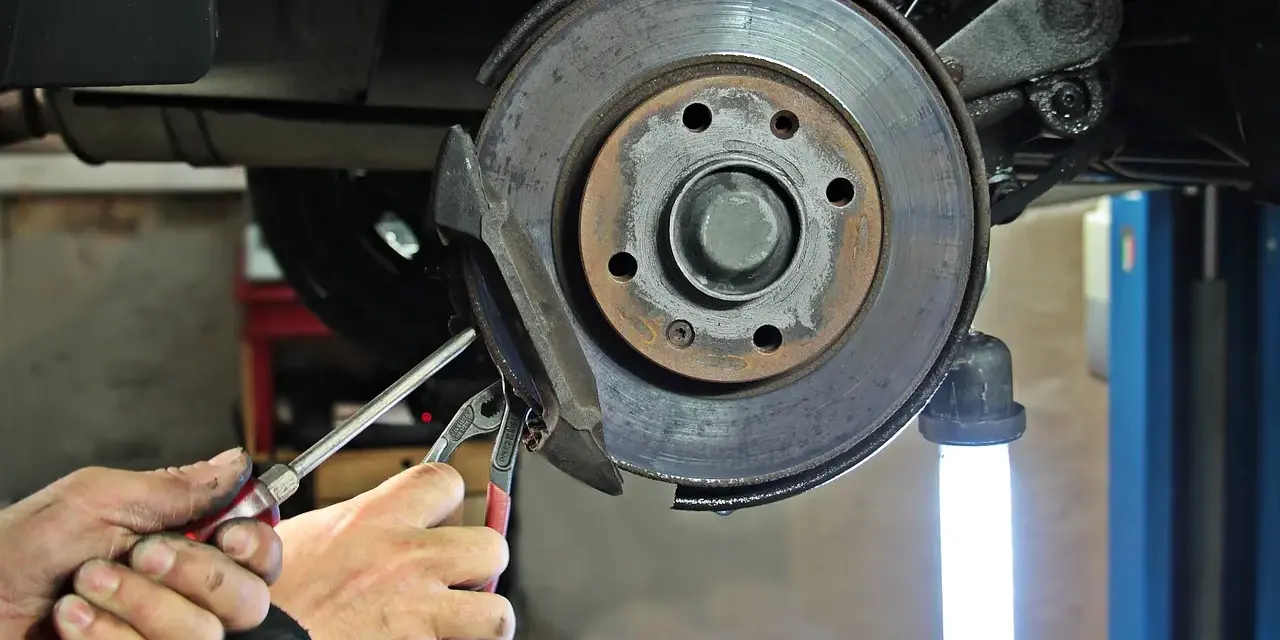 Dłonie mechanika z narzędziami przy hamulcu tarczowym samochodu.