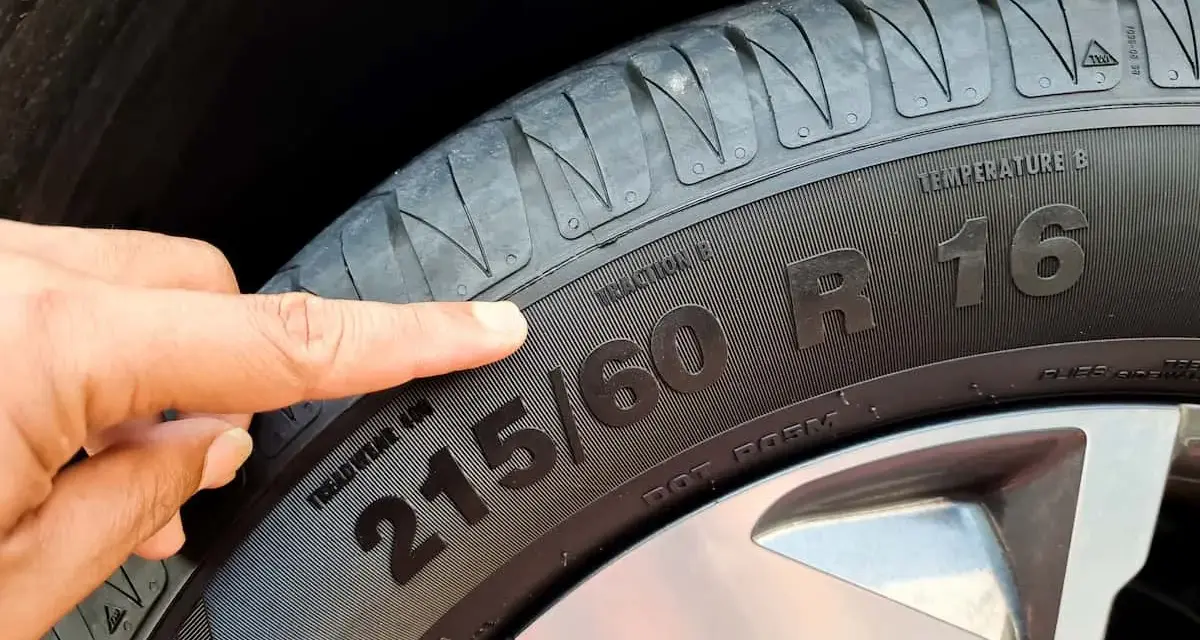 Palec wskazuje na oponę, gdzie widoczny jest rozmiar 215/60 R16. To ważny element, który określa indeks prędkości opon.