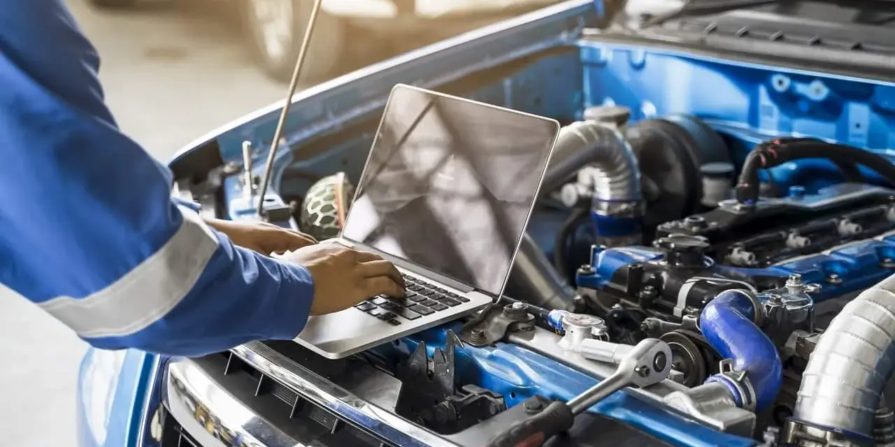 Mechanik w niebieskim kombinezonie wykonuje mapowanie silnika na laptopie, analizując jego pracę.