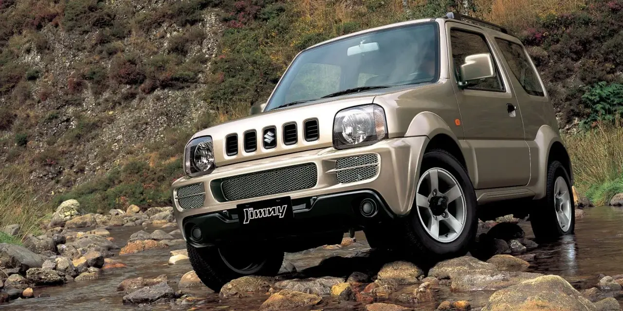 Złoty Suzuki Jimny pokonuje kamienisty strumień. Sprawdź suzuki jimny cena i możliwości terenowe tego kultowego auta.