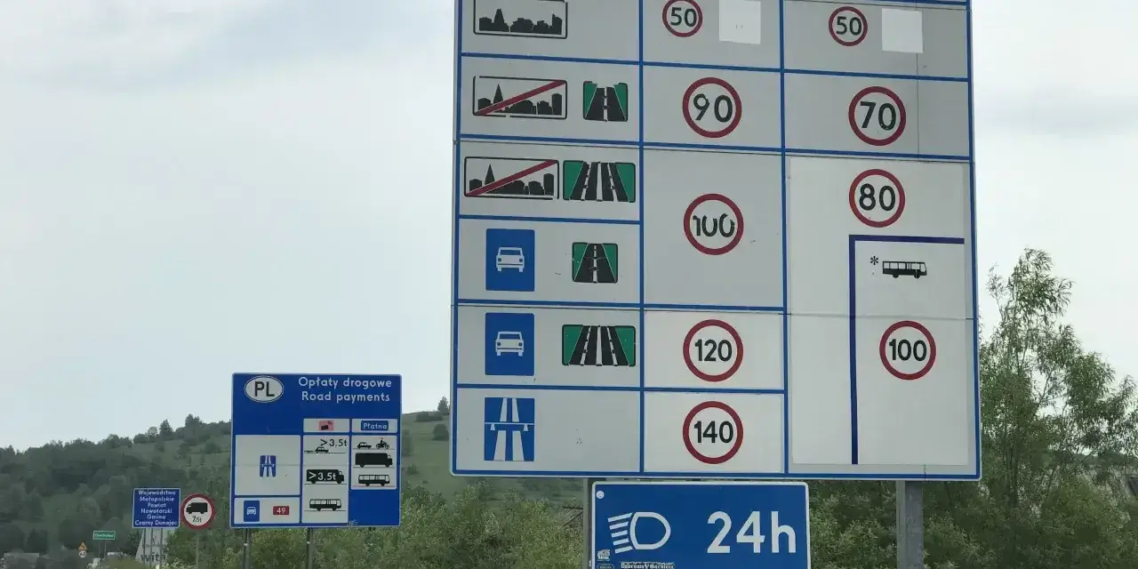 Znaki drogowe przy drodze dwujezdniowej informują o opłatach i limitach prędkości.