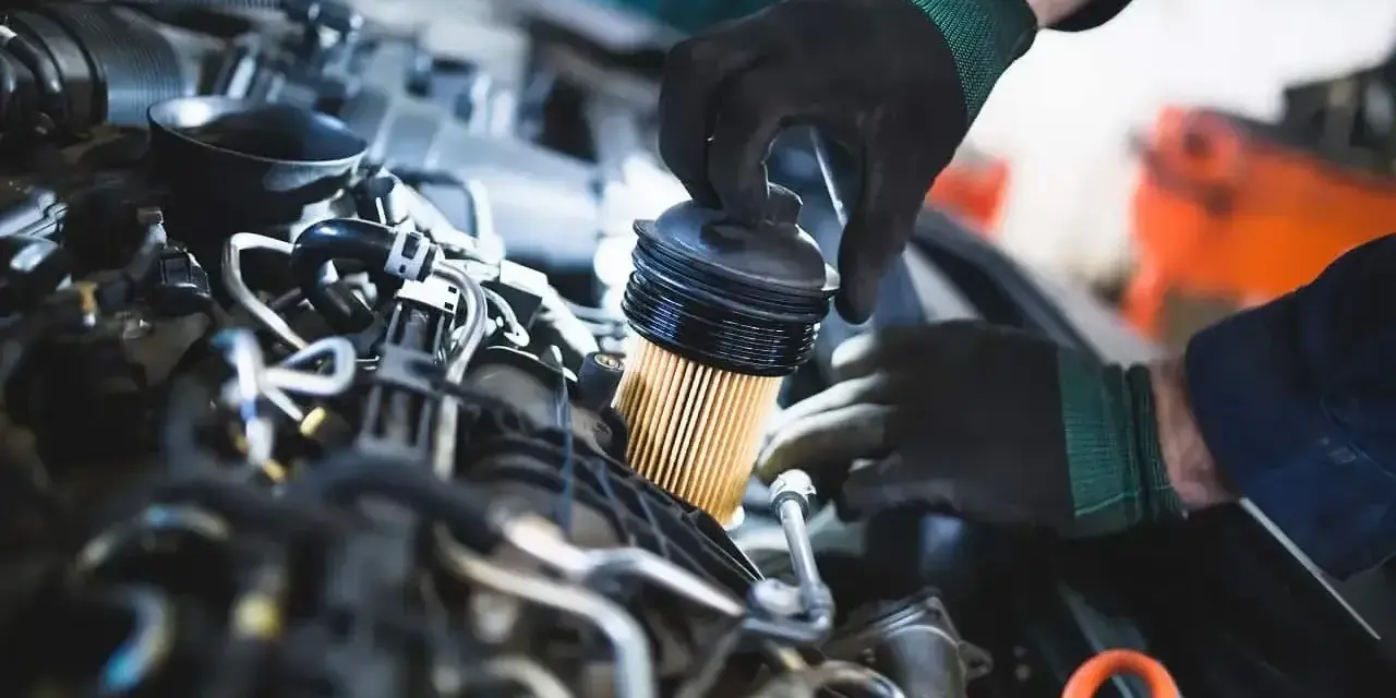 Mechanik w czarnych rękawiczkach dokonuje wymiany filtra paliwa w silniku samochodu.