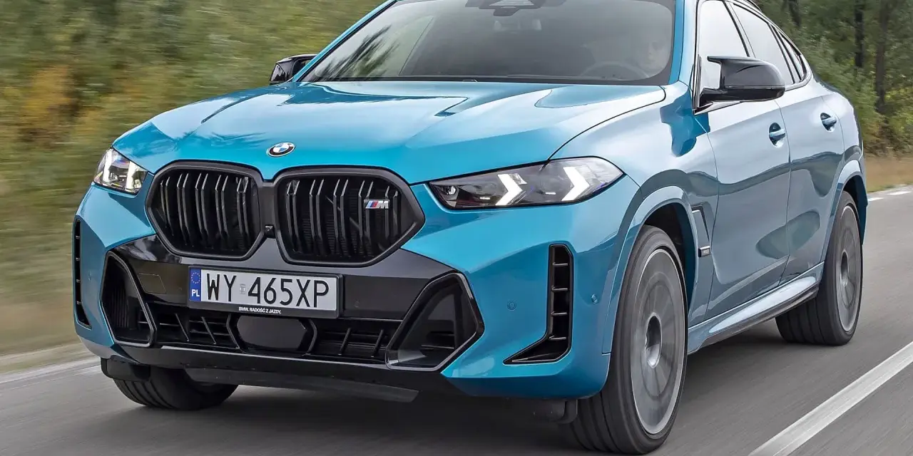 Niebieskie x6 BMW M na drodze, z rozmytym tłem lasu.