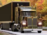 Błyszczący Kenworth W900 z przyczepą jedzie drogą wśród jesiennych drzew.