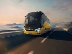 Żółty setra autobus pędzi po autostradzie wśród chmur i gór, w stronę mostu.