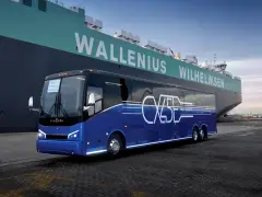 Niebieski autokar Van Hool CX45 z napisem "ZERO EMISSIONS" stoi przy ogromnym statku Wallenius Wilhelmsen.