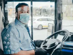 Kierowca autokaru w masce i rękawiczkach za kierownicą. Zapytaj o wynajem autokaru cena.