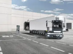 Ciężarówka Terberg z naczepą stoi przy ładowarce elektrycznej przed magazynem.