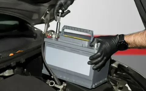 Mechanik w czarnych rękawiczkach montuje akumulator samochodowy, przygotowując go do regeneracji.
