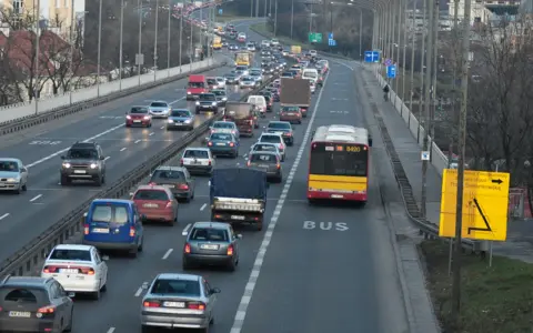 Autobus jedzie pasem dla autobusów. Wokół ruch samochodowy.