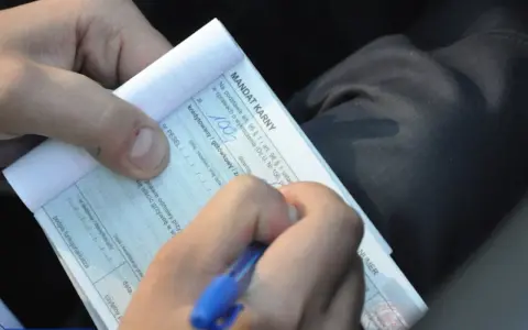 Ręka pisze mandat karny. Kierowca otrzymał mandat za brak przeglądu technicznego pojazdu.