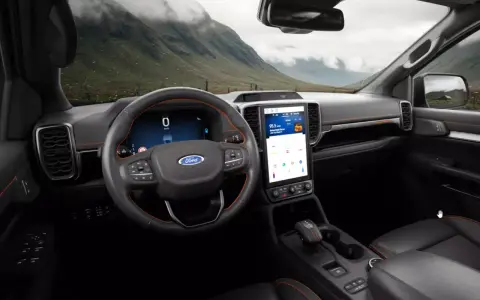 Wnętrze nowoczesnego Ford SUV z dużym ekranem dotykowym i cyfrowymi zegarami. Widok na górzysty krajobraz przez przednią szybę.