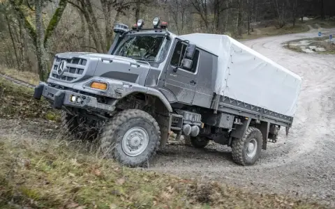 Szary Mercedes Zetros z plandeką pokonuje trudny teren leśnej drogi.