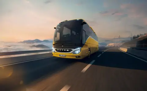 Żółty setra autobus pędzi po autostradzie wśród chmur i gór, w stronę mostu.