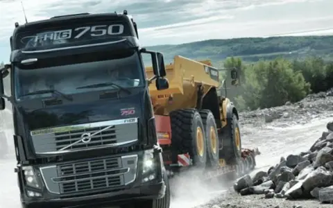 Ciężarówka Volvo FH16 750 z naczepą przewozi żółty wozidło przegubowe przez kamieniołom.