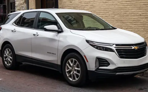 Biały Chevrolet Equinox stoi zaparkowany na brukowanej ulicy, obok ceglanego budynku.