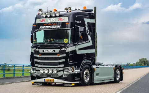 Czarna Scania V8 z szarymi pasami, z napisem "TERMOTRAFIK" i licznymi światłami, gotowa do trasy.
