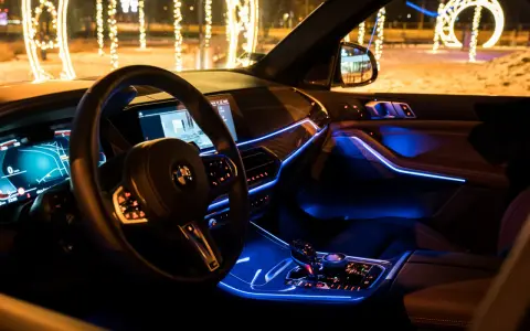 Wnętrze luksusowego BMW x5 nocą, oświetlone niebieskim ambientowym światłem. Za oknem świąteczne iluminacje.