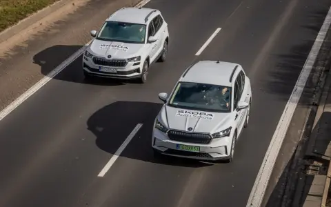 Dwa białe samochody Skoda Auto Szkoła jadą po drodze, gdzie obowiązuje ruch lewostronny.
