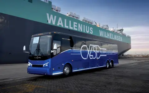 Niebieski autokar Van Hool CX45 z napisem "ZERO EMISSIONS" stoi przy ogromnym statku Wallenius Wilhelmsen.