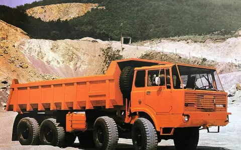 Pomarańczowy wywrotka Tatra 813 z zapasowym kołem na pace, gotowa do pracy w kamieniołomie.