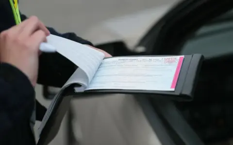 Funkcjonariusz wypisuje mandat karny po kolizji drogowej. Dokument zawiera numer sprawy i szczegóły wykroczenia.