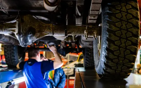 Mechanik bada podwozie terenowego Forda 4x4. Widoczna masywna oś i bieżnik opony.