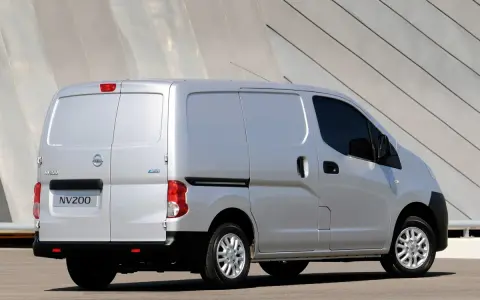 Srebrny Nissan NV200, wszechstronny van, zaparkowany przed nowoczesnym budynkiem.