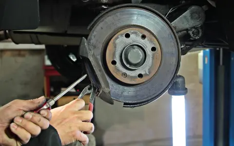 Dłonie mechanika z narzędziami przy hamulcu tarczowym samochodu.