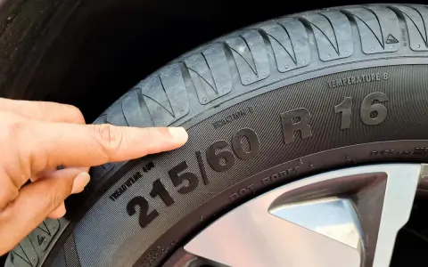 Palec wskazuje na oponę, gdzie widoczny jest rozmiar 215/60 R16. To ważny element, który określa indeks prędkości opon.