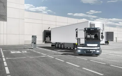 Ciężarówka Terberg z naczepą stoi przy ładowarce elektrycznej przed magazynem.