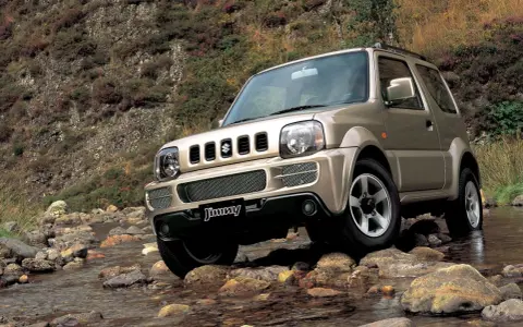 Złoty Suzuki Jimny pokonuje kamienisty strumień. Sprawdź suzuki jimny cena i możliwości terenowe tego kultowego auta.