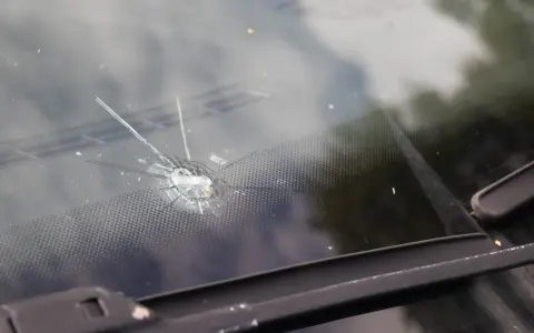 Odprysk na szybie samochodowej, przypominający gwiazdę, z widocznymi pęknięciami i drobnymi odłamkami szkła.