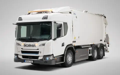 Biała śmieciarka Scania Streamline z niebieskim akcentem na grillu i pomarańczowymi światłami ostrzegawczymi na dachu.
