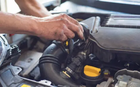 Ręce mechanika pracują przy silniku samochodu. Widoczny jest czarny przewód dolotowy i żółta zakrętka. p0101.