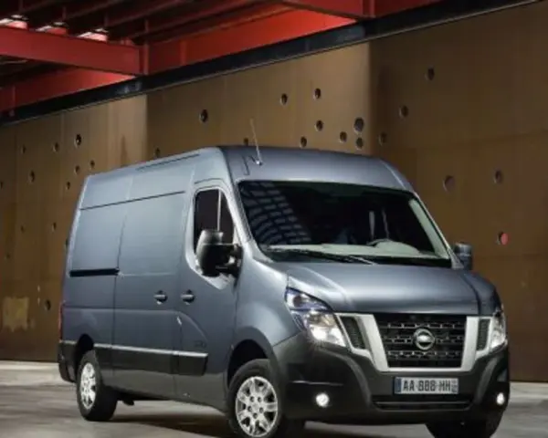 Szary Nissan NV400 stoi przed brązową, perforowaną ścianą w industrialnym wnętrzu.