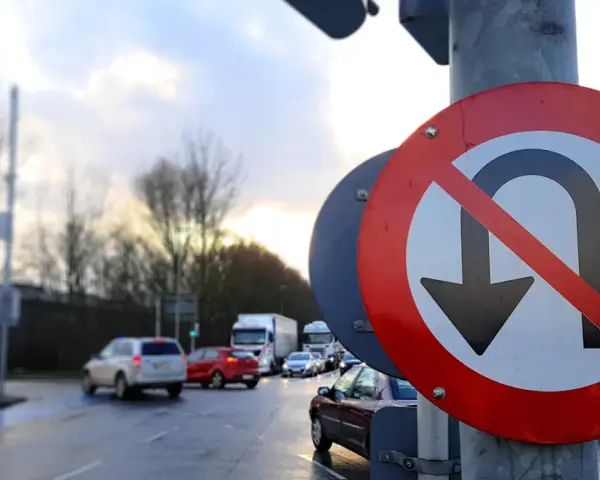 Znak zakazu zawracania na skrzyżowaniu. Samochody stoją w deszczu, czekając na zielone światło.