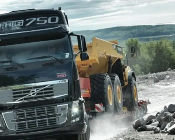 Ciężarówka Volvo FH16 750 z naczepą przewozi żółty wozidło przegubowe przez kamieniołom.