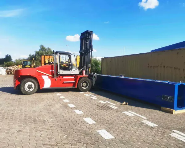 Czerwony wózek widłowy przygotowuje się do przeładunku długiego, niebieskiego elementu. To przykład sprawnego cross dockingu.