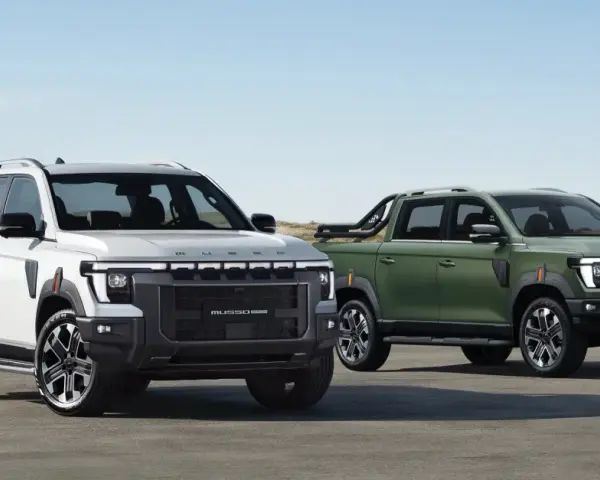 Dwa SsangYong pickup: biały i zielony, stojące na tle plaży i wydm.