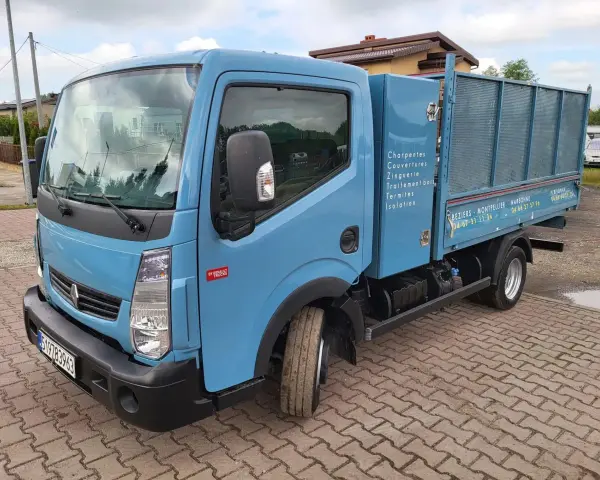 Niebieska ciężarówka Renault Maxity z otwartą skrzynią ładunkową, zaparkowana na brukowanym podjeździe.