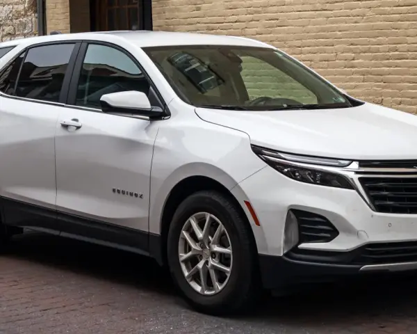 Biały Chevrolet Equinox stoi zaparkowany na brukowanej ulicy, obok ceglanego budynku.