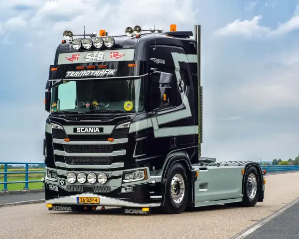 Czarna Scania V8 z szarymi pasami, z napisem "TERMOTRAFIK" i licznymi światłami, gotowa do trasy.