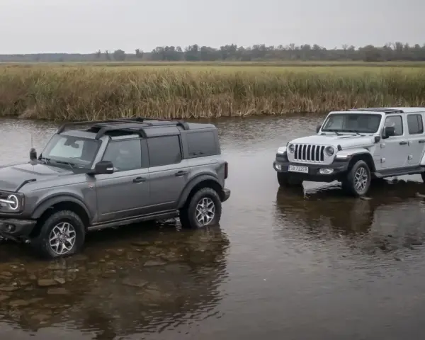 Szary Ford Bronco i biały Jeep SUV stoją w płytkiej wodzie, gotowe na przygodę.